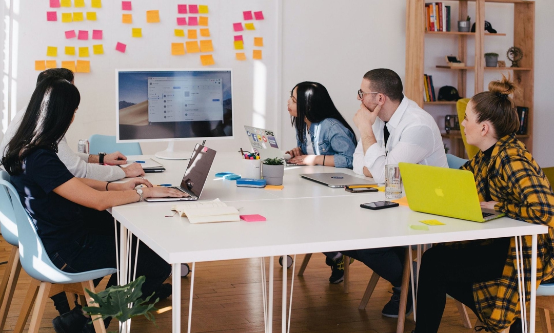 A group of office workers gather around a monitor in a meeting