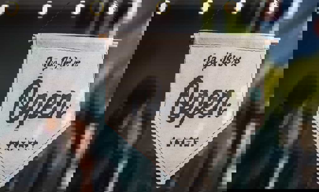 Two people celebrate behind a store open sign