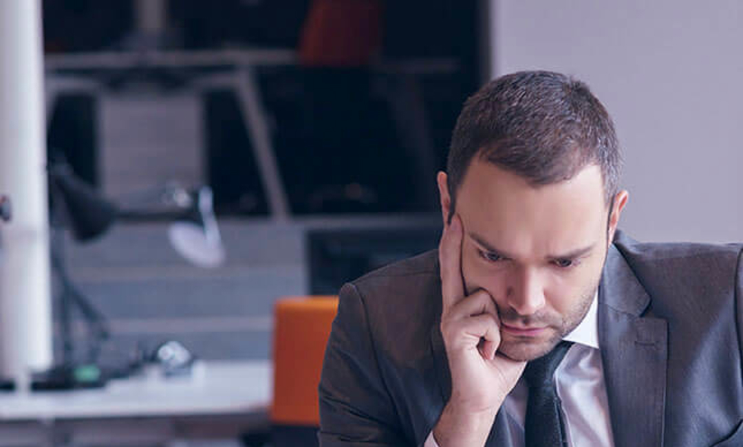 Man sitting in front of a laptop with is hand on his face